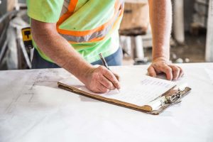 A construction worker with freckled arms writes down notes on a piece of paper